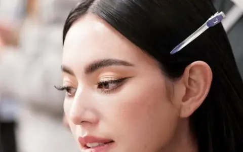 Primer plano de una mujer con ojos rasgados, delineado de gato y cabello oscuro recogido con una pinza.