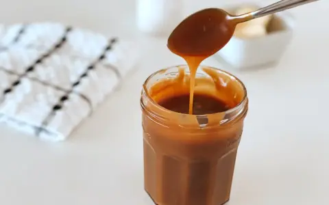 Une cuillère verse un caramel beurre salé liquide dans un pot en verre. Parfait pour une recette gourmande.