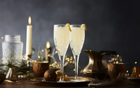 Två eleganta glas med en uppfriskande drink med gin och prosecco, dekorerade med citronskal. Stämningsfull belysning med ljus och ljusslingor skapar en festlig atmosfär.