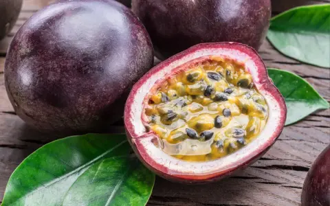 Dunkle, runde Früchte liegen auf Holz. Eine davon ist aufgeschnitten und zeigt das saftige Fruchtfleisch mit Kernen – eine köstliche Passionsfrucht Maracuja.