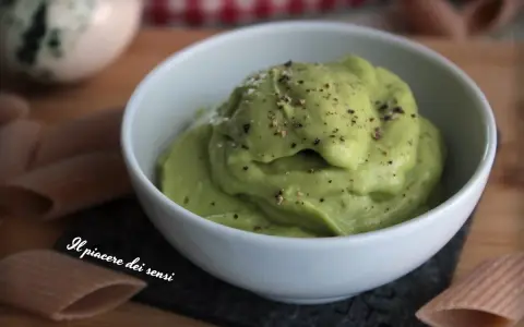 Una ciotola bianca piena di vellutata crema di avocado, cosparsa di pepe nero macinato. Accanto, pasta integrale.