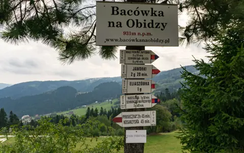 Tablica z drogowskazami na szlak na Radziejową. W tle górzysty krajobraz Beskidu Sądeckiego.