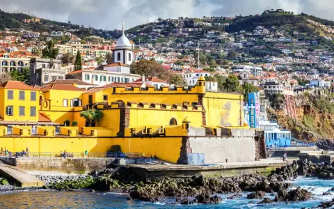 Gelbe Festung in Funchal, Madeira, mit Häusern, die sich den Hang hinaufziehen.