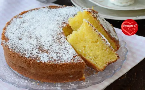 Una soffice torta allo yogurt, cosparsa di zucchero a velo, con due fette tagliate per mostrare la sua morbidezza. Perfetta per la colazione o la merenda.