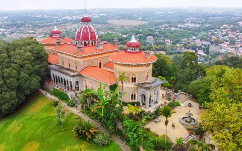 Der Monserrate Palast thront auf einem Hügel, umgeben von üppiger Vegetation und einer malerischen Stadt. Seine roten Dächer und Türmchen sind ein Blickfang.