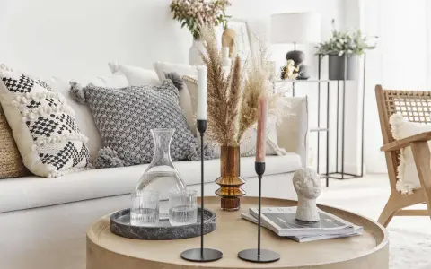 Un accogliente salotto bohemien con cuscini decorativi, un vaso di erba della pampa e candele su un tavolino rotondo.