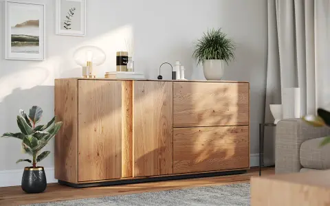 Drewniana komoda Nuis z dwoma drzwiczkami i szufladami, ozdobiona roślinami i lampą, tworzy przytulną atmosferę.