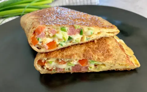 Keto tortilla z jajkiem, warzywami i wędliną, pokrojona na pół, prezentuje apetyczny przekrój.