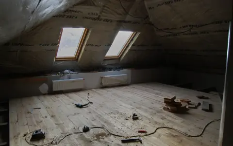 Grenier en cours d'aménagement, avec pare-vapeur fibre de bois, deux fenêtres de toit et un plancher en bois brut. Outils de bricolage au sol.