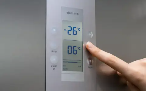 Palec naciska przycisk na panelu lodówki no frost. Wyświetlacz pokazuje -26°C i 06°C.