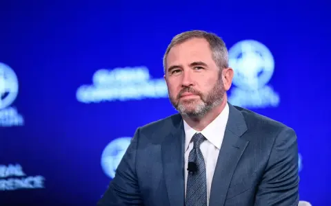 Brad Garlinghouse, CEO Ripple, w niebieskim garniturze, z brodą, na tle niebieskiej sceny z logo Global Conference.