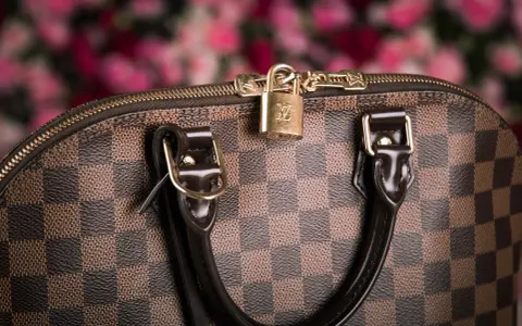 Dettaglio di una borsa Louis Vuitton, icona dell'azienda, con il classico motivo a scacchiera e un lucchetto dorato.