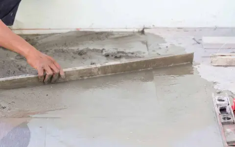 Ręka wyrównuje świeży beton, tworząc idealnie gładką podłogę na gruncie.