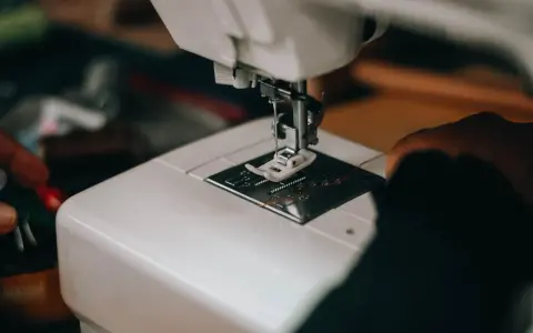 Zbliżenie na białą maszynę do szycia, gdzie igła jest gotowa do pracy, ale nić jest luźna, sugerując, że maszyna do szycia nie wiąże ściegu.