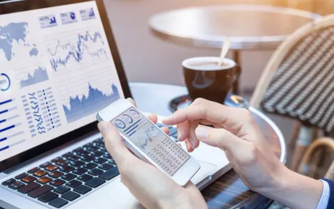 Manos revisando gráficos financieros en un teléfono móvil y portátil, gestionando el bbva net cash.