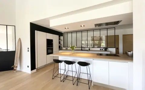 Cuisine moderne avec îlot central, plan de travail en bois et verrière industrielle. Une belle idée cuisine avec verriere pour un espace lumineux.