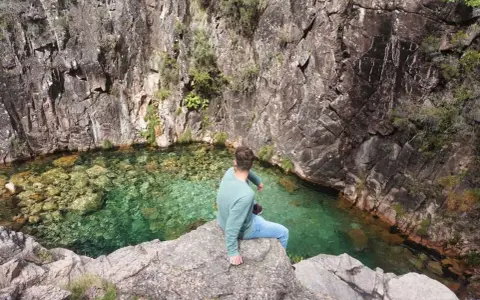 Mann sitzt auf Felsen am kristallklaren Wasser des Peneda-Gerês-Nationalparks.