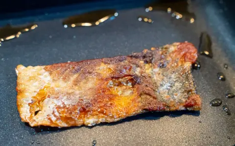 Ein Stück Lachs braten in der Pfanne, die Haut ist knusprig und goldbraun, das Fleisch saftig.