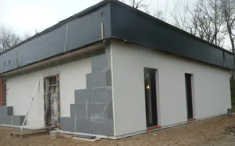 Budowa domu ze styropianu w trakcie. Widoczne bloczki, okna i dach przykryty czarną folią.