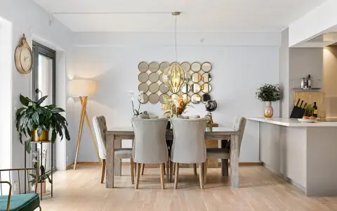 Comedor elegante con mesa de madera y sillas tapizadas, sobre un suelo sisal. Decoración con espejos circulares y lámpara colgante.