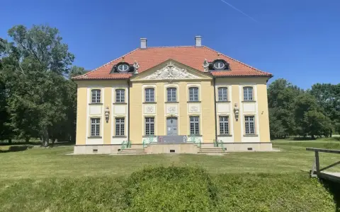 Piękny, żółty pałac w Choroszczy z czerwonym dachem, otoczony zielenią i błękitnym niebem.