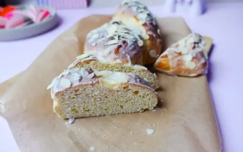 Süßer Hefekuchen ohne Zucker, mit zarter Glasur und Mandelblättchen bestreut, auf Backpapier angerichtet.