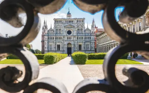 La Certosa di Pavia, un capolavoro rinascimentale, vista attraverso un cancello decorato. Un percorso conduce alla maestosa facciata.