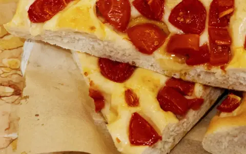 Saftige Focaccia Pomodoro mit geschmolzenem Käse und sonnengetrockneten Tomaten, auf Backpapier serviert.