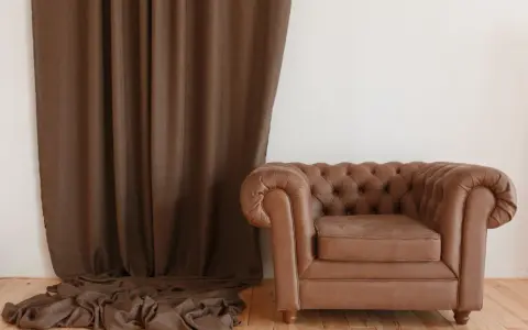 Butaca de cuero marrón estilo Chester junto a cortina marrón. ¿Cuánto cuesta tapizar una butaca como esta?