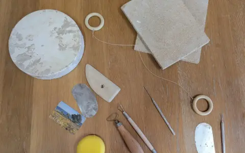 Keramikverktyg och en lerklump på ett träbord. Här finns allt för att visa vad man kan dreja: skärtråd, träformar, metallverktyg och en svamp.