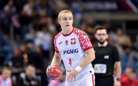 Młody zawodnik w białej koszulce z orłem i numerem 4, gotowy do rzutu piłką ręczną.