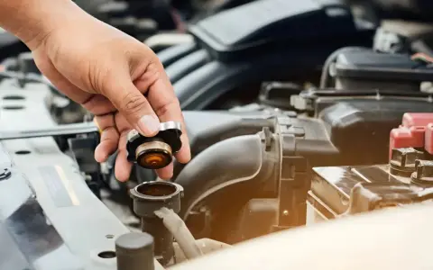 Hand removing radiator cap. This image might be relevant when researching radiator hose replacement cost.