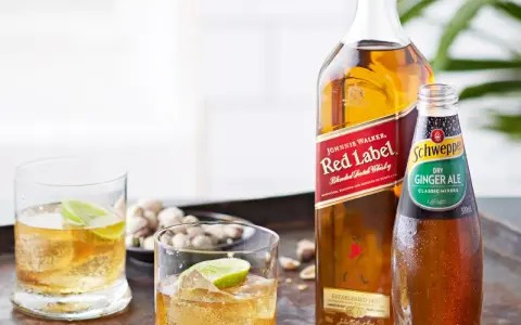 Butelka Johnnie Walker Red Label, butelka Schweppes Ginger Ale i dwa drinki z lodem i limonką.