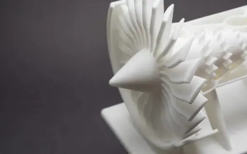 A detailed white model of a jet engine's turbine, showcasing intricate blades, likely created by a laser sintering machine.