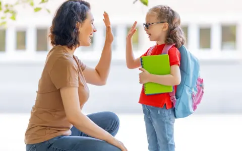 Madre y hija se dan un choque de manos, un momento de crianza positiva antes de ir a la escuela.