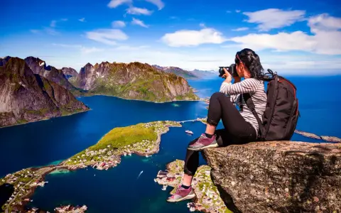 En fotograf fångar de dramatiska vyerna över Lofoten sevärdheter, med branta berg och en idyllisk by vid det blå havet.