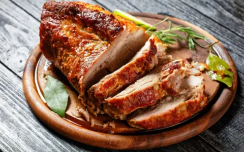 Un rôti de porc au four, coupé en tranches, sur une planche en bois. Le temps cuisson rôti de porc au four moelleux est parfait pour ce plat savoureux.