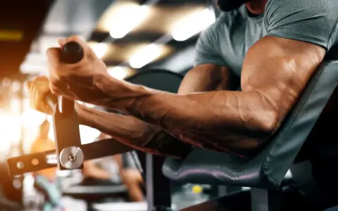 Ein Mann trainiert seinen Bizeps-Muskel an einem Gerät im Fitnessstudio. Die Adern treten deutlich hervor.