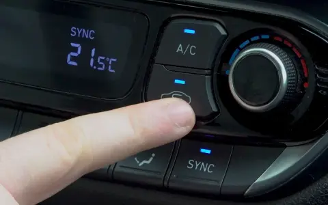 Dedo presionando el botón recirculacion aire del climatizador del coche.