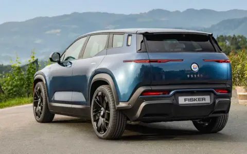 Tylna część niebieskiego elektrycznego SUV-a Fisker Ocean na tle gór i zieleni.