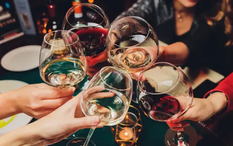 Hände heben Gläser mit Weiß- und Rotwein zum Anstoßen. Die ideale trinktemperatur für den Wein wird genossen.