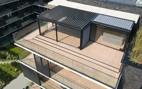 Nowoczesny taras na dachu z przeszklonym pawilonem i pergolą. Drewniana podłoga i szklane balustrady tworzą elegancką przestrzeń.