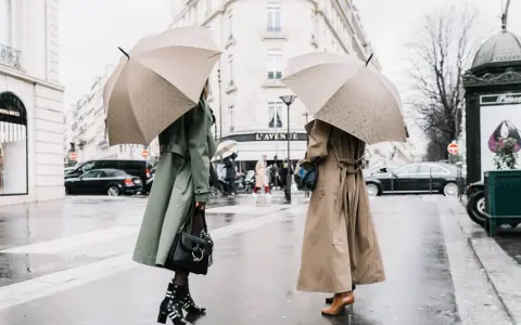 Dos mujeres con paraguas lucen elegantes gabardinas, como se llaman las chaquetas largas, en un día lluvioso en París.