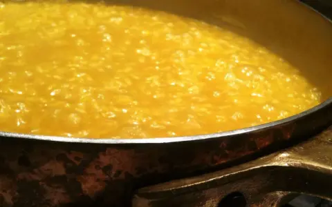 Un cremoso risotto alla milanese che sobbolle in una pentola di rame, pronto per essere gustato.
