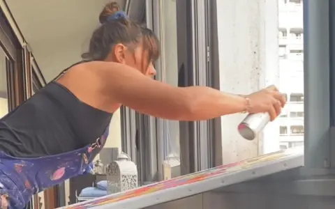 Une artiste applique du vernis sur sa peinture acrylique colorée, protégeant ainsi son œuvre.
