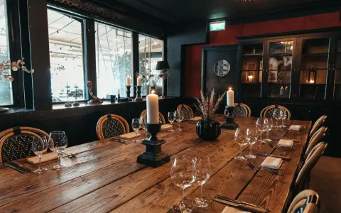 Ett elegant chambre séparée med ett långt träbord, dukat för middag med levande ljus och vinglas.