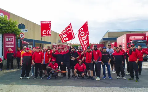 Un gruppo di lavoratori BRT, con bandiere rosse, manifesta per migliorare le condizioni di lavoro. Le loro opinioni su lavorare in Bartolini sono chiare.
