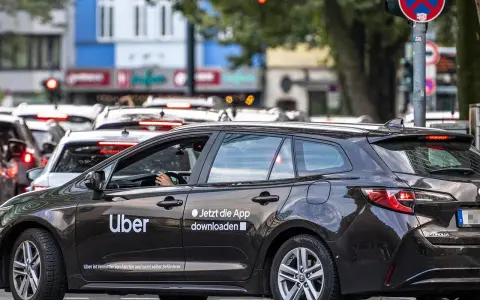 Ein dunkler Uber-Kombi steht im Stau. Die Aufforderung "Jetzt die App downloaden" ist gut sichtbar.