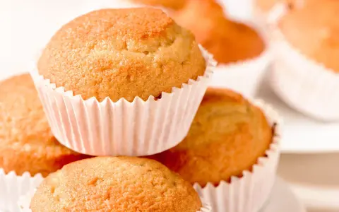 Ein Stapel goldbrauner, veganer Muffins in weißen Papierförmchen. Sie sehen köstlich und frisch gebacken aus.
