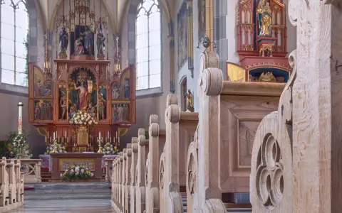 Drewniane ławki w kościele św. Jana w Warszawie, prowadzące do ołtarza z bogatymi zdobieniami i figurami.